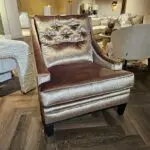 Brown velvet tufted armchair on a dark wood floor in a furniture showroom with beige sofas in the background