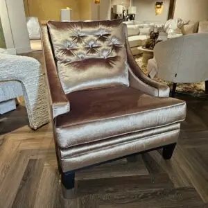 Brown velvet tufted armchair on a dark wood floor in a furniture showroom with beige sofas in the background