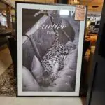 Black-and-white Cartier Paris ad showing a leopard-print garment draped over a tufted sofa in a showroom display