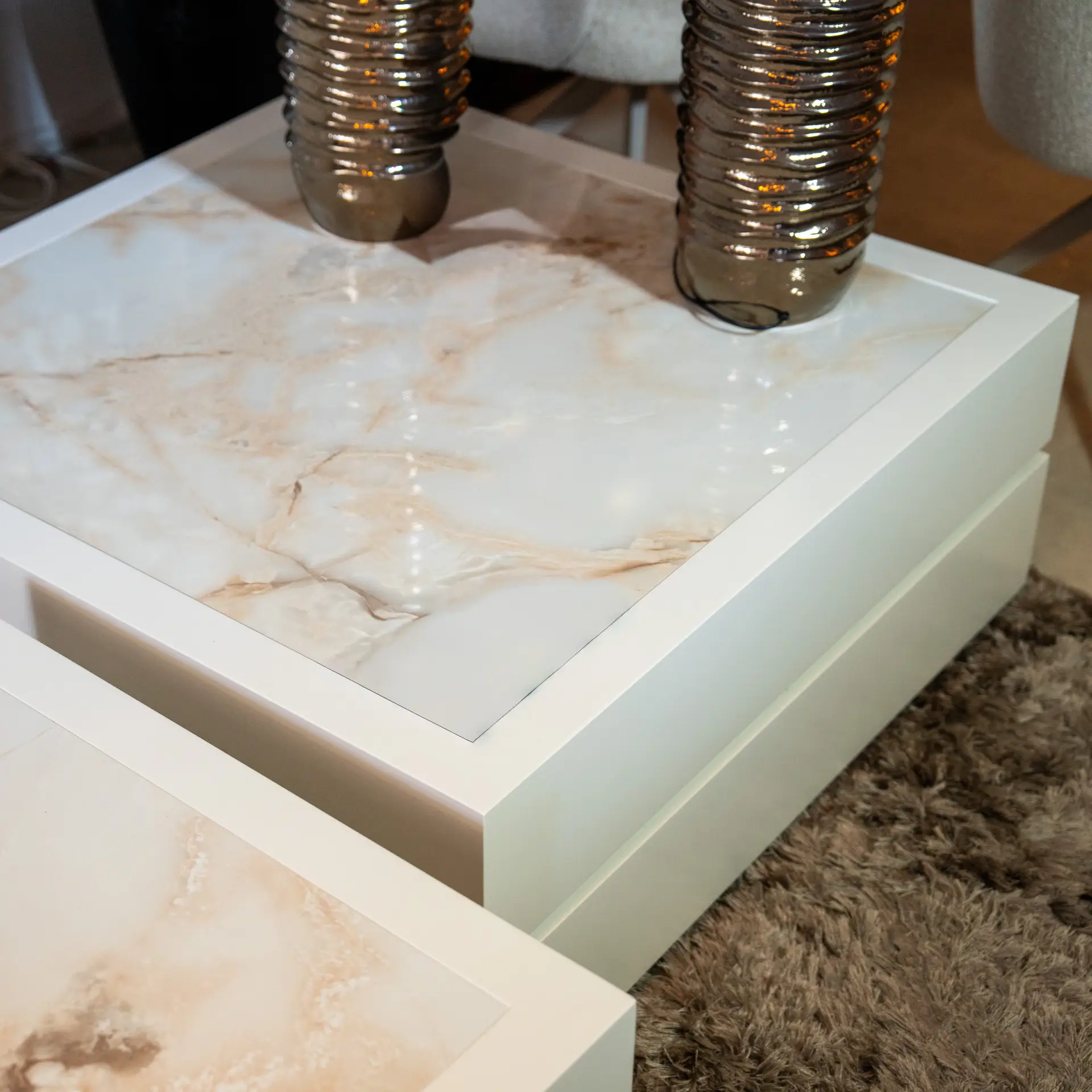 Close-up of a marble tabletop with a white frame, showing twisted metallic legs and a beige shag carpet in the background.