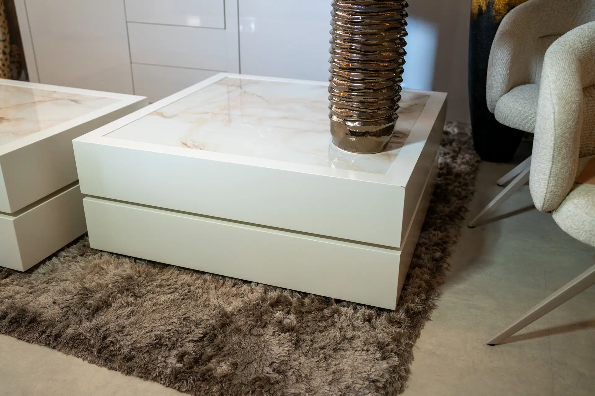 White marble-top coffee table with a tall ribbed metallic vase in a contemporary living room setting
