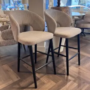 Two beige curved-back bar stools with black legs in a furniture showroom.