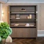 Open dark wooden shelving unit with a small stack of books and a black decorative rock on the top shelf, against a patterned tile wall.