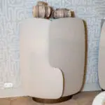 Two beige, curved-back chairs overlap in front of a gray patterned wall with looping shapes.]
