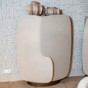 Two beige, curved-back chairs overlap in front of a gray patterned wall with looping shapes.]