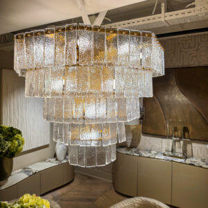 Chandelier made of textured glass panels hanging from ceiling in a showroom kitchen display, with warm lighting on gold tones.