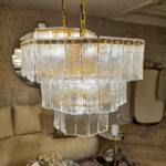 Crystal chandelier with textured glass panels hanging from gold chains in a showroom setting