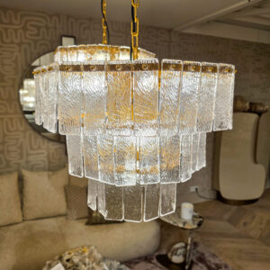 Crystal chandelier with textured glass panels hanging from gold chains in a showroom setting