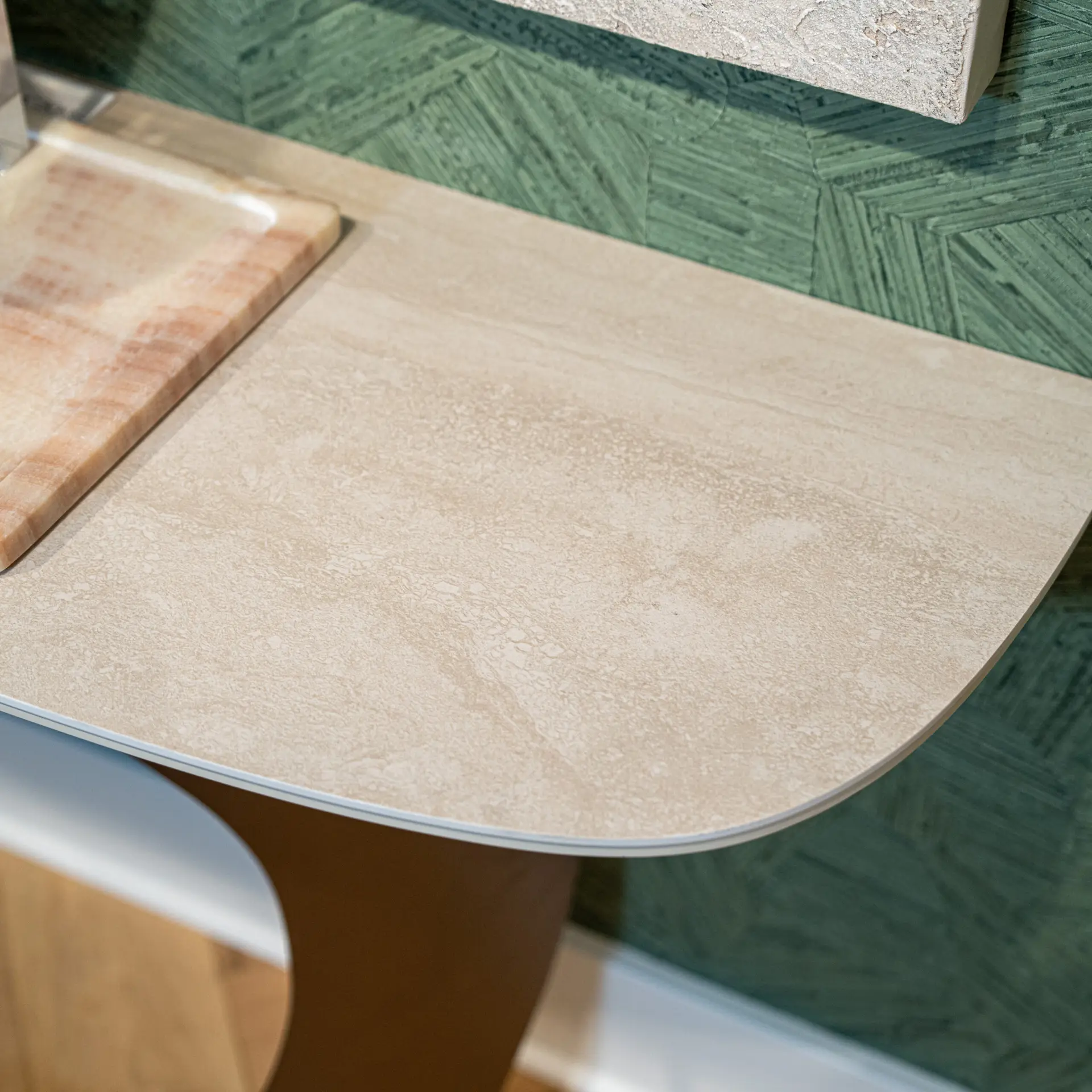Curved beige kitchen island countertop with textured speckled surface and a green patterned wall in the background.