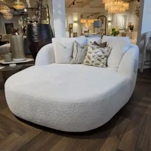 Curved light-gray textured sofa with multiple decorative pillows in a well-lit furniture showroom.