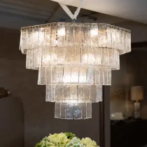 Crystal chandelier with rectangular textured glass panels hanging from a white cord in a dim room, foreground hydrangea blooms.