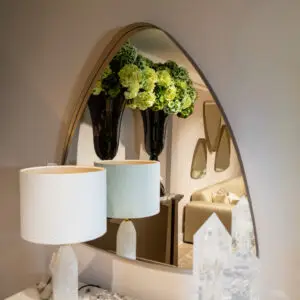 Arched wall mirror reflecting pale green hydrangea bouquets in tall black vases on a console.