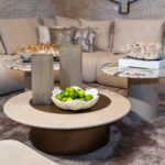 White scalloped bowl filled with bright limes on a round coffee table in a modern living room with a gray sofa and textured cushions in the background.
