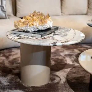 Crystal cluster or quartz geode resting on a closed book atop a marble coffee table in a living room setting, with a blurred sofa in the background.