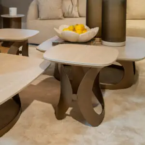 Round beige coffee tables arranged in a living room with a white scalloped bowl of lemons atop a book centerpiece.