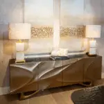 Showroom living room scene with beige lamps flanking a stone-accent wall and brown cabinetry beneath.