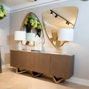 Wooden sideboard with two round wall mirrors, green hydrangea arrangements, and two lamps on top.