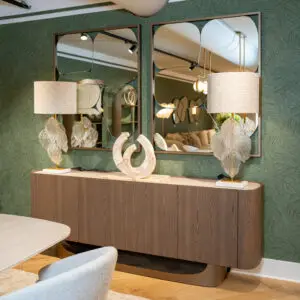 Showroom interior with green textured wall, framed mirrors, and beige lamps on a wooden cabinet display.