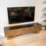 Flat-screen TV mounted on a white textured wall above a dark glossy media cabinet, with a remote on the right side of the cabinet.
