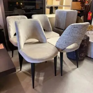 Set of light gray upholstered dining chairs with curved backs and black tapered legs, arranged in a furniture showroom display.