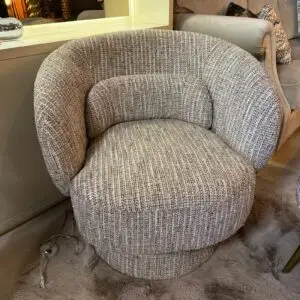 Round gray textured chair with a matching ottoman in a living room, with a clear wine glass on the shaggy rug nearby.
