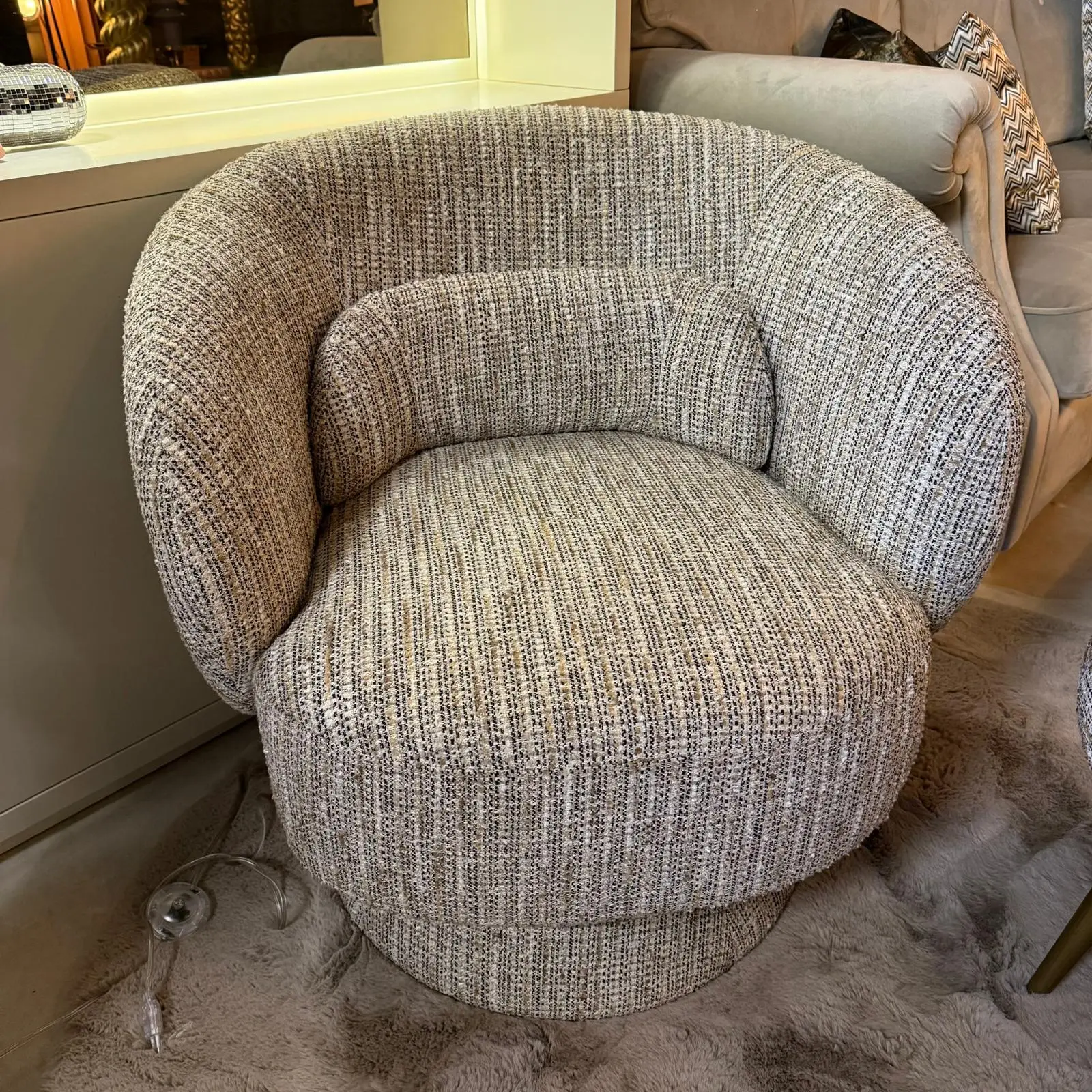 Round gray textured chair with a matching ottoman in a living room, with a clear wine glass on the shaggy rug nearby.