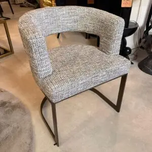 A tweed upholstered armchair with curved back and metal sled legs in a showroom setting