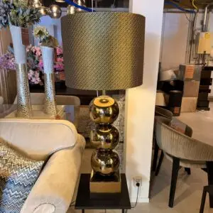Gold mirrored ball lamp with a black geometric shade on a square black table, in a showroom setting.