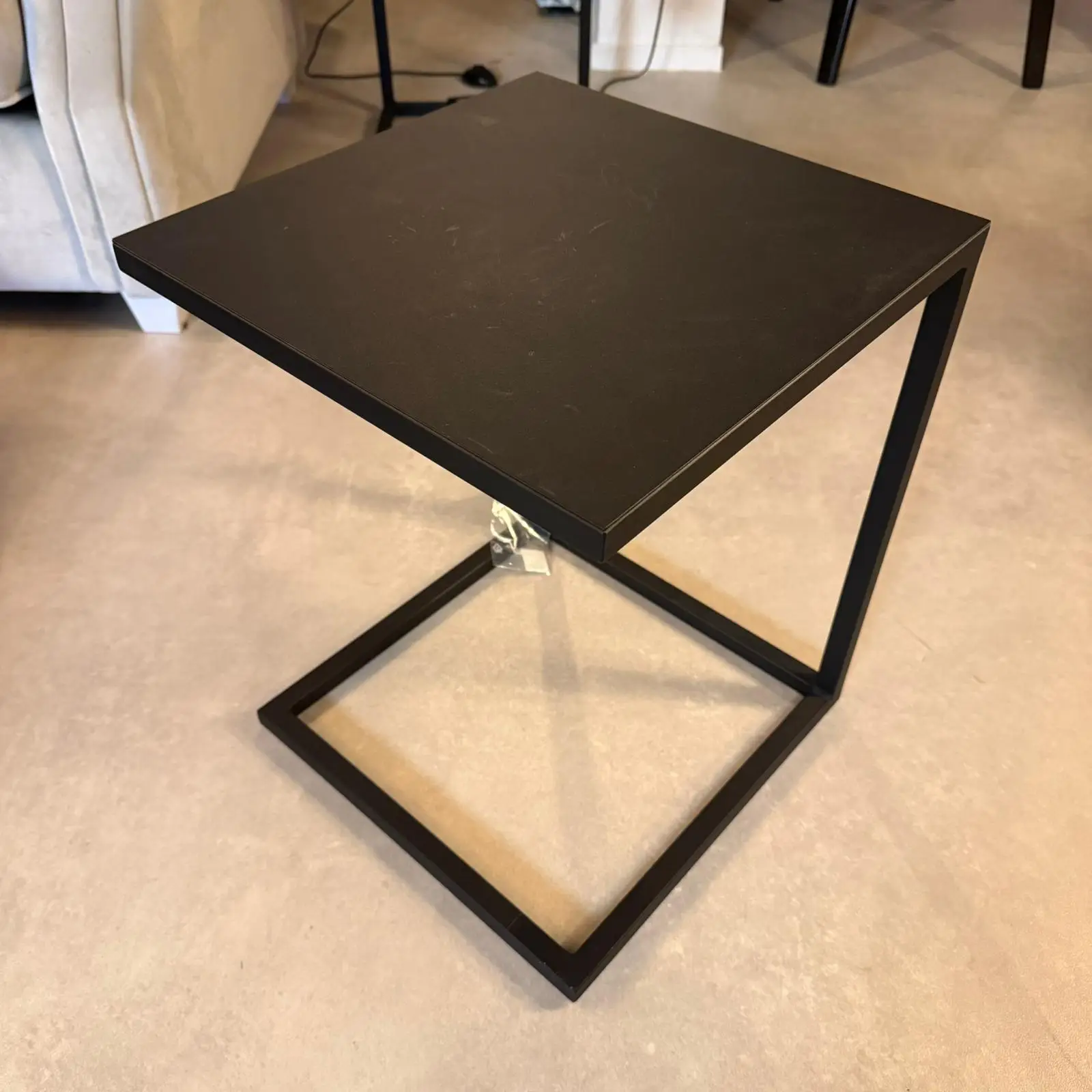 Modern black square-top side table with a minimalist metal frame on a beige floor