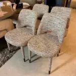 Pair of gray-tweed upholstered armchairs with curved arms on a showroom floor, adjacent to a glass table.