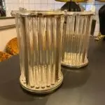 Two tall chrome and glass cylinder lamps with vertical glass rods on a dark surface in a showroom setting