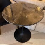 Round black marble-top side table with a central pedestal base, showing white veining on the surface.