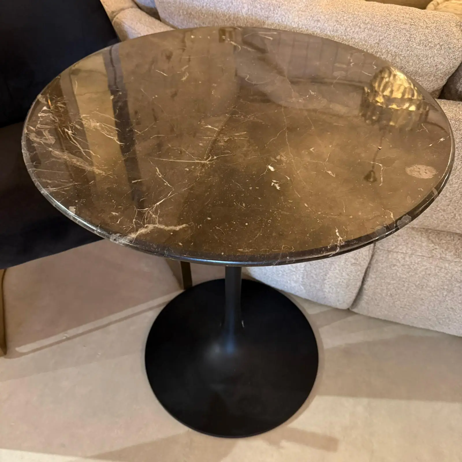Round black marble-top side table with a central pedestal base, showing white veining on the surface.