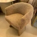 Beige textured upholstered armchair with rounded arms, shown in a showroom setting next to a sink and display cabinet.