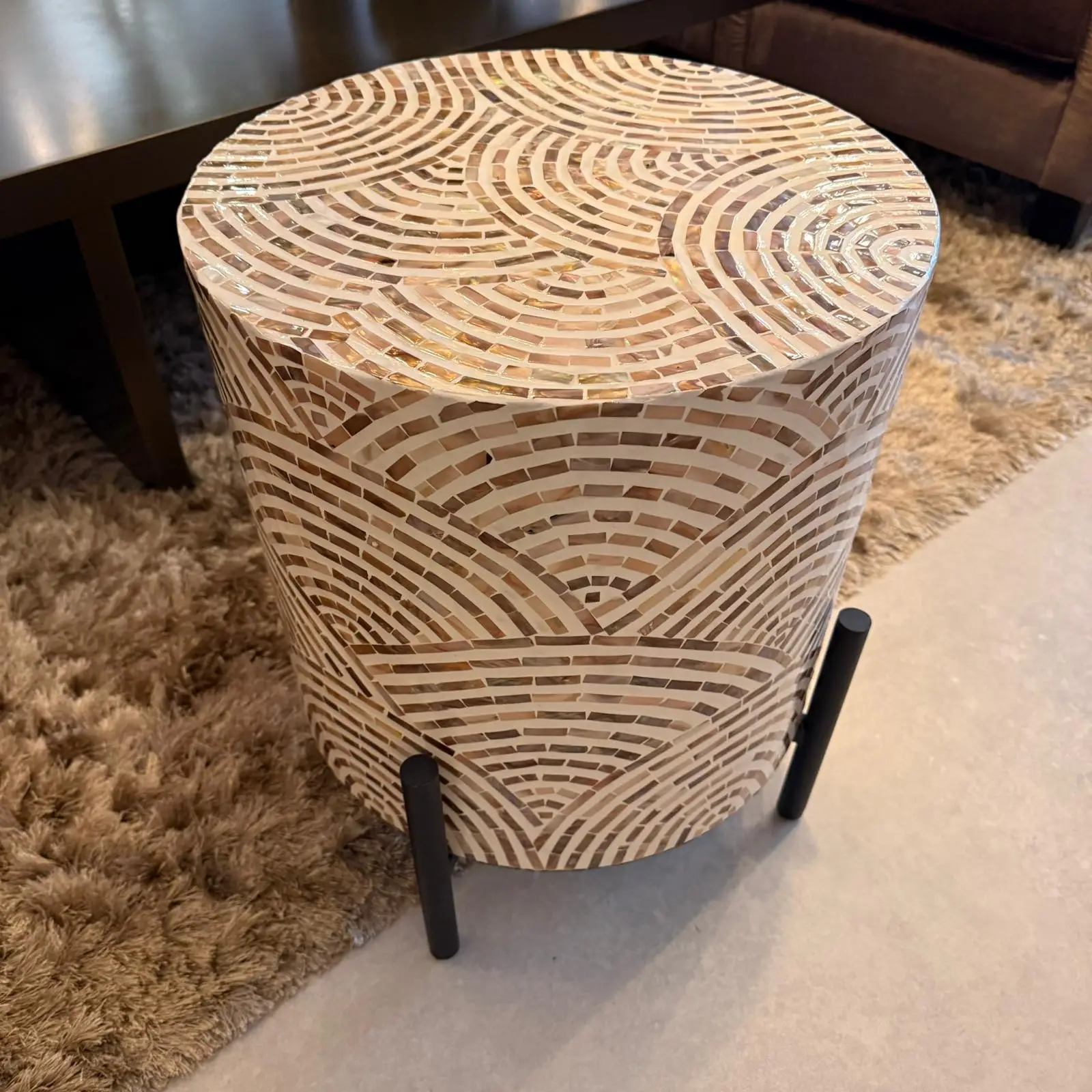 Round mosaic-tiled side table with beige and cream curved tile patterns in a living room setting on a shaggy rug.