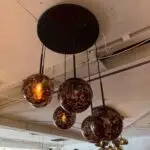 Cluster of dark amber glass globe pendant lights hanging from a black circular ceiling plate in an industrial interior setting.