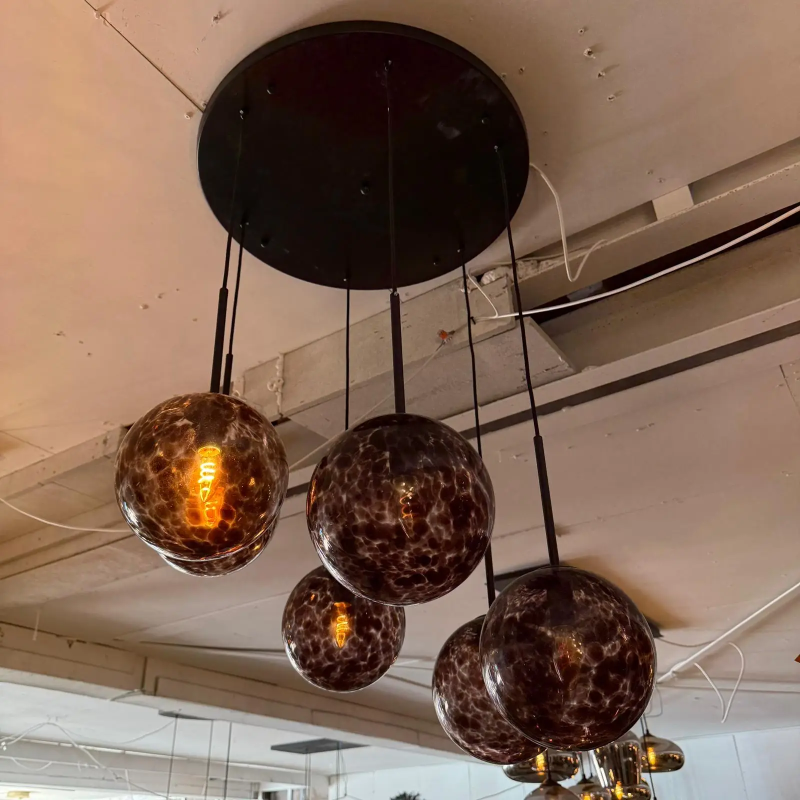 Cluster of dark amber glass globe pendant lights hanging from a black circular ceiling plate in an industrial interior setting.