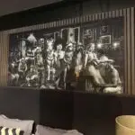 Large black-and-white mural of cowboys and a horse in a bar scene, mounted on a dark wall with wooden slats