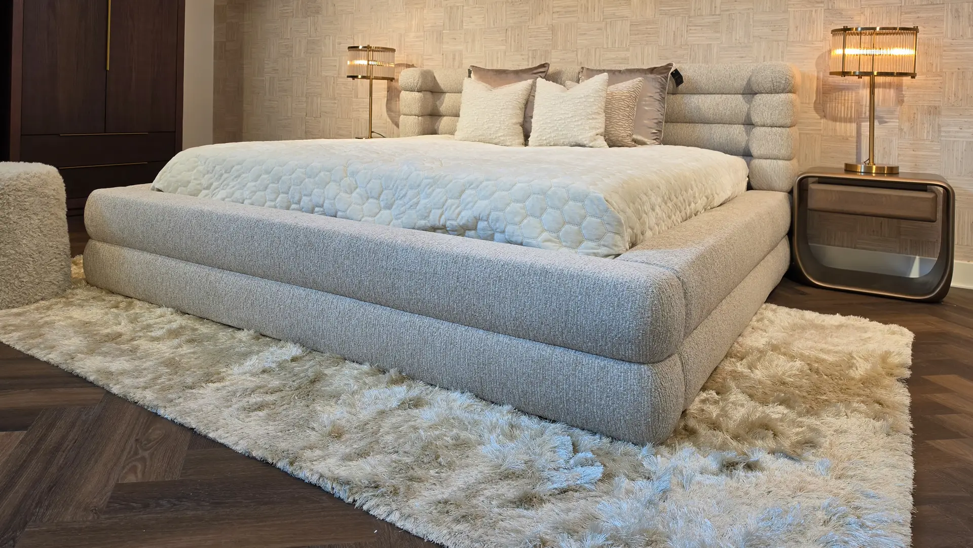 Luxurious gray platform bed with a textured quilt and fluffy pillows in a modern bedroom with a shag rug.