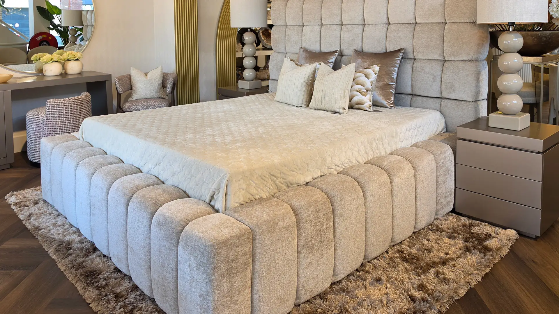 Luxurious gray upholstered bed with a tall, tufted headboard, matching nightstands, and plush pillows in a neutral-toned bedroom.
