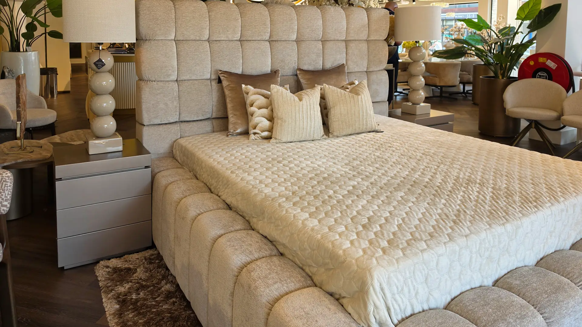 Beige upholstered bed with a tall tufted headboard and coordinating pillows in a showroom setting