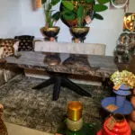 Showroom scene with a marble table, tufted leather seats, tall potted plants, and colorful stacked vases labeled SALE on tags to the right.