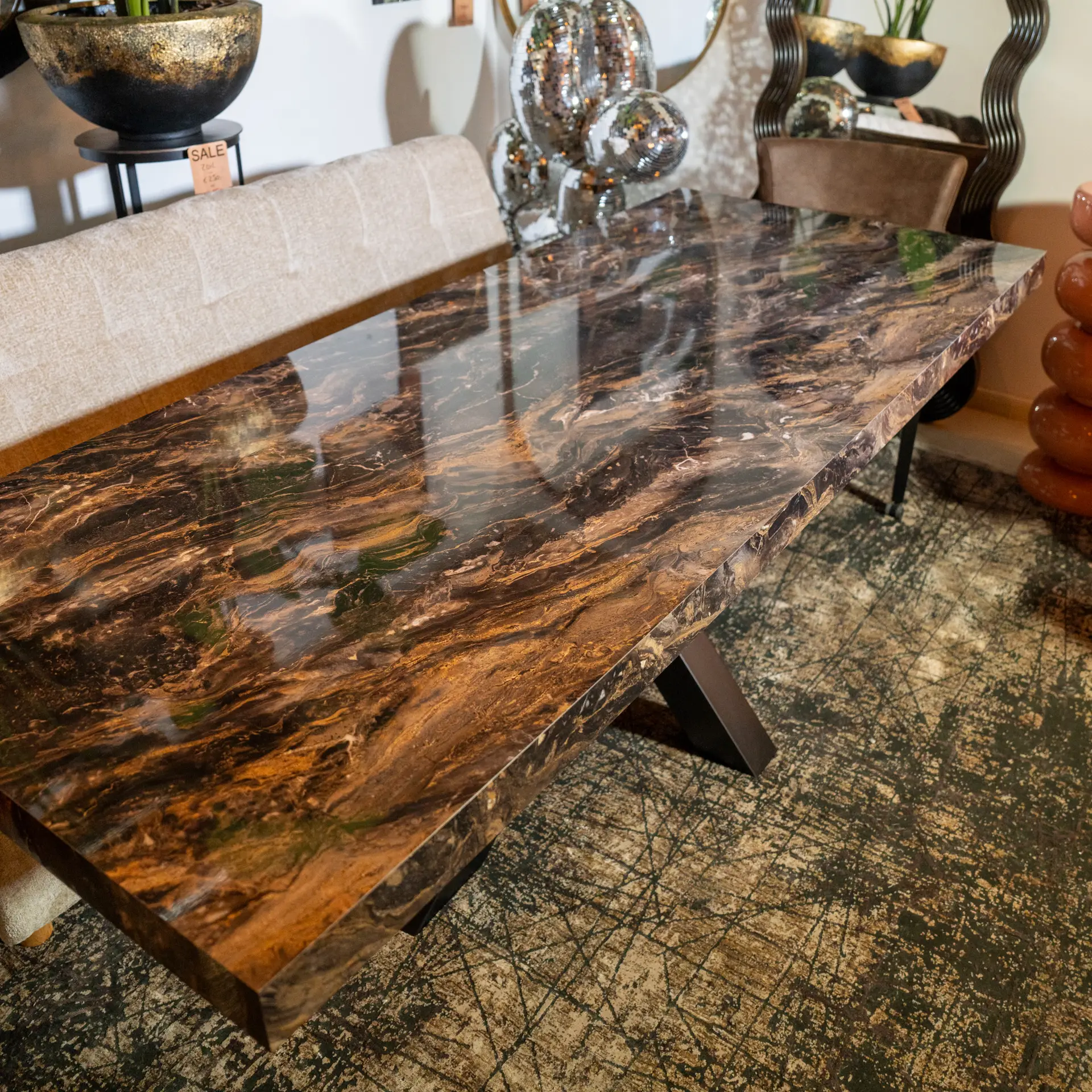 Interior showroom scene featuring a dark brown marble countertop, beige upholstered seating, and decorative glass orb sculptures with plants on a stand in the background.