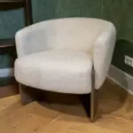 Beige upholstered armchair with wooden legs on a wooden floor, against a green textured wall.