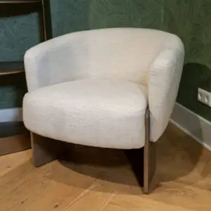 Beige upholstered armchair with wooden legs on a wooden floor, against a green textured wall.