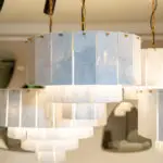 White marble rectangular panels hanging from gold chains, forming a modern chandelier-like installation.