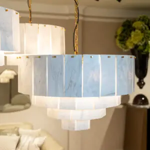 Circular chandelier with white marble panels and gold chains hanging above a bedroom bed in a warm-lit room.