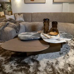 Cozy living room with a beige sectional, textured pillows, and a plush brown throw on a shaggy carpeted floor. Two amber glass vases sit on a marble coffee table in front of the sofa.