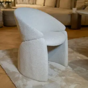 Close-up of a light gray textured fabric chair with a curved back in a living room setting.