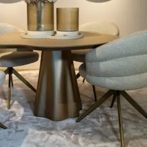 Round dining table with a dark brown pedestal base and two gray upholstered chairs on a textured carpet, seen from a low angle.